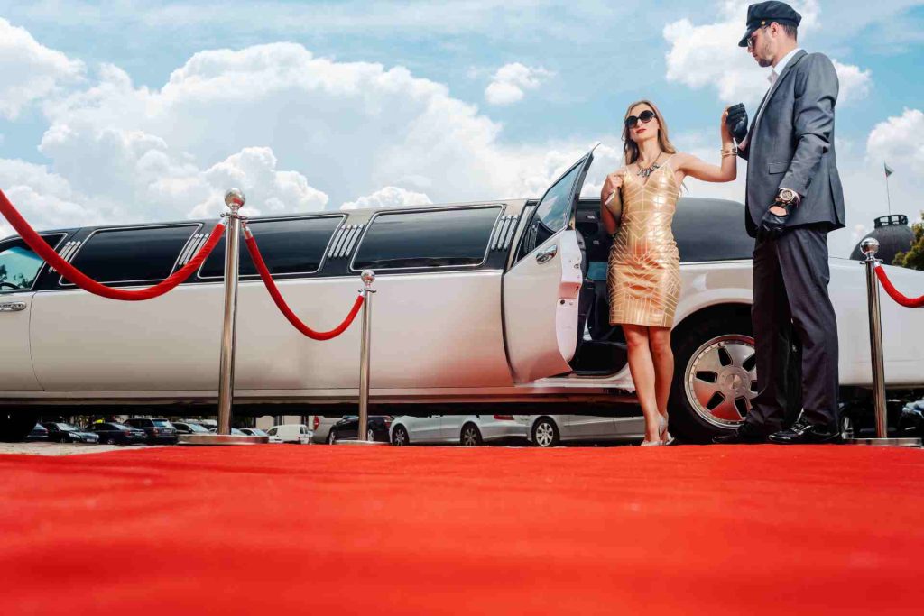 A man and woman pose beside a limousine on a red carpet, exuding elegance and glamour at a prestigious event.