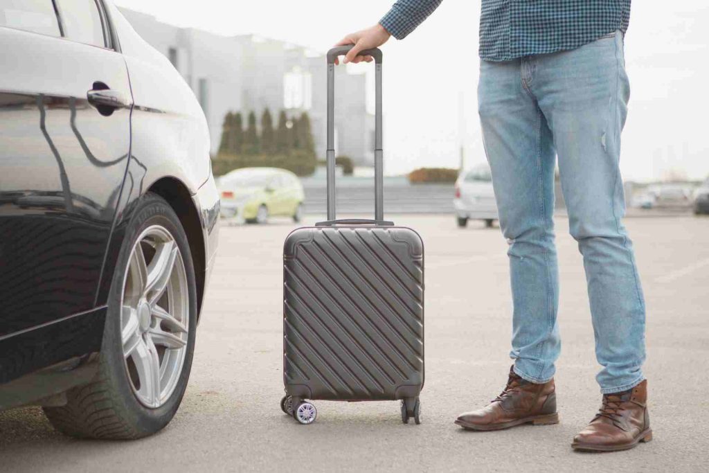 A man stands beside a car, holding a suitcase, ready for travel or departure.