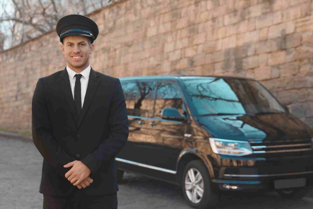 A man in a suit and tie stands beside a black van, exuding professionalism and readiness for business.