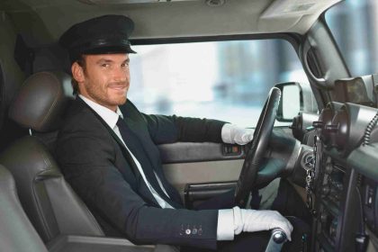 A man in a suit and tie seated in the driver's seat of a car.